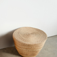 Woven stool on a concrete floor with a white wall background
