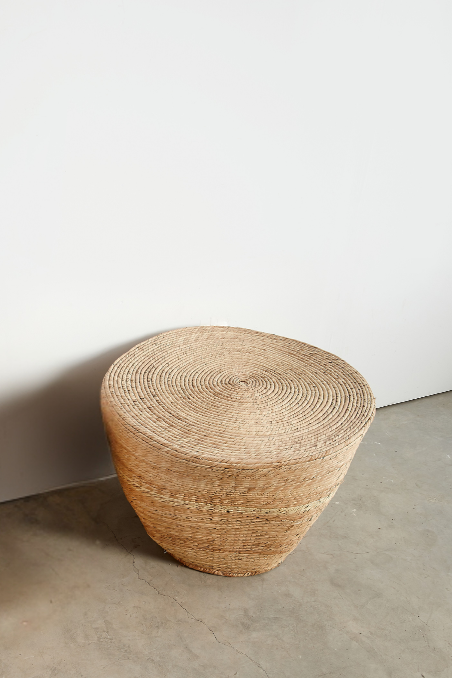 Woven stool on a concrete floor with a white wall background