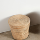 Woven straw stool against a plain wall on a concrete floor