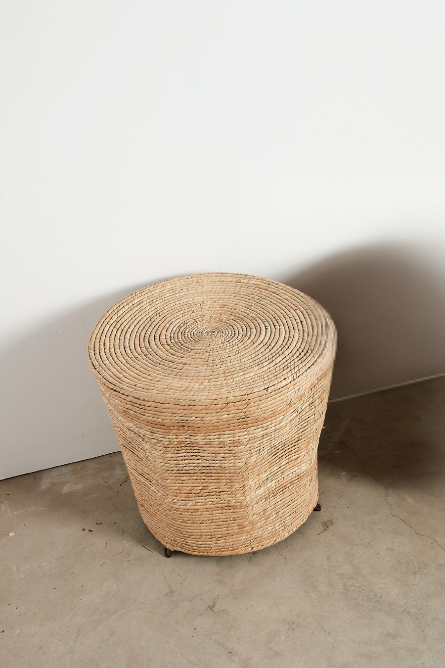 Woven straw stool against a plain wall on a concrete floor