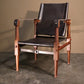 Sophisticated campaign chair with a polished mahogany wood structure and luxurious black leather upholstery, standing on a sleek grey floor with a shadowy background that highlights its sleek design and fine craftsmanship.