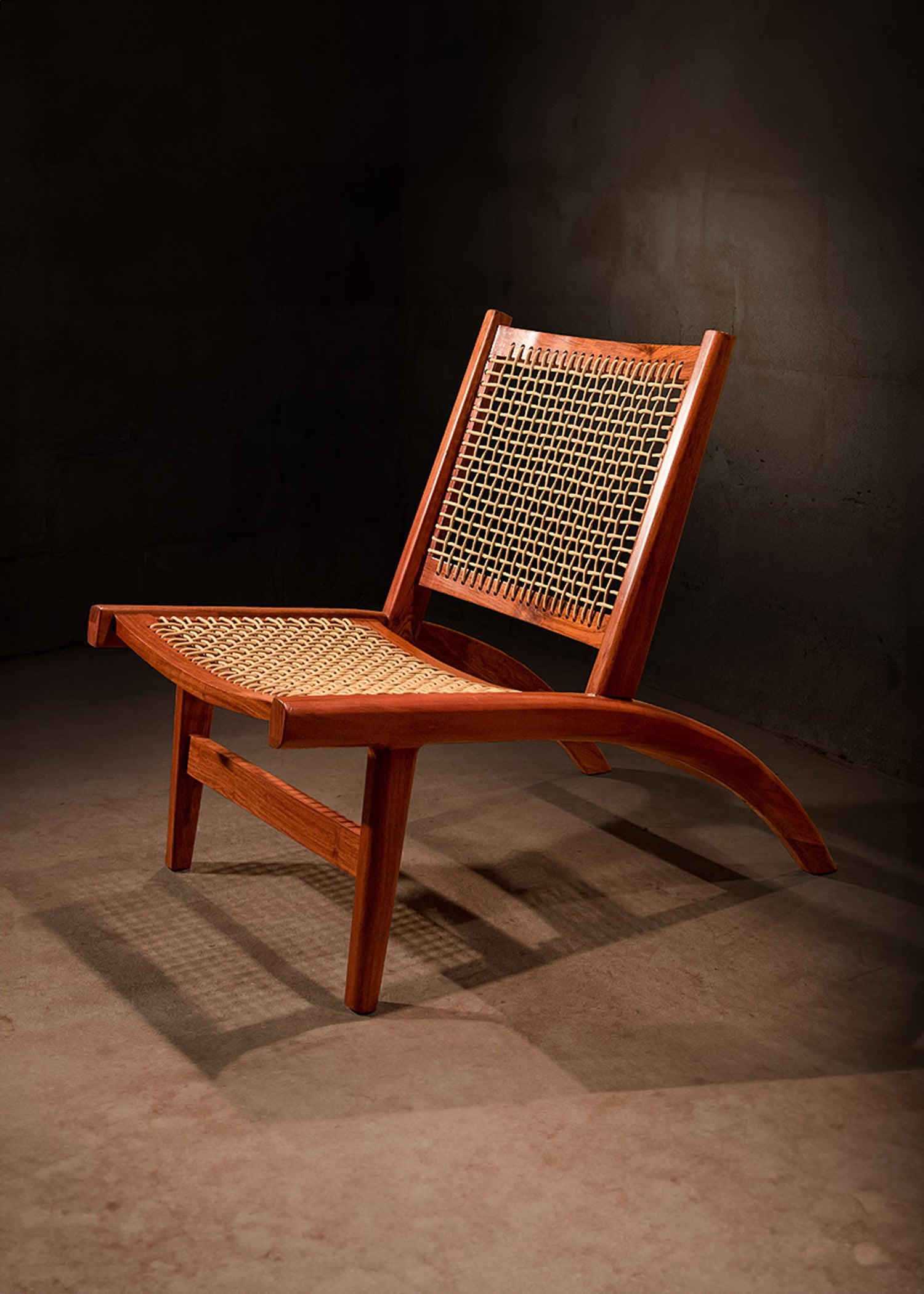 Elegant teak wood chair with a seat and backrest intricately woven from yacht sail rope, displayed against a darkened concrete backdrop, highlighting the chair's exquisite curves and the contrasting textures that evoke luxury and comfort