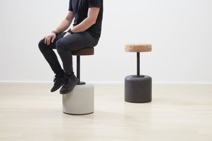 Designer Laurie Wiid van Heerden demonstrates the scale of Kanju's Wiid Swivel Cork and Concrete Barstool, offering a real-world perspective on its size and ergonomic design. This image captures Laurie seated on the innovative barstool, which combines the warmth of cork with the strength of concrete, showcasing the piece's functional elegance and sustainable approach to modern furniture design.
