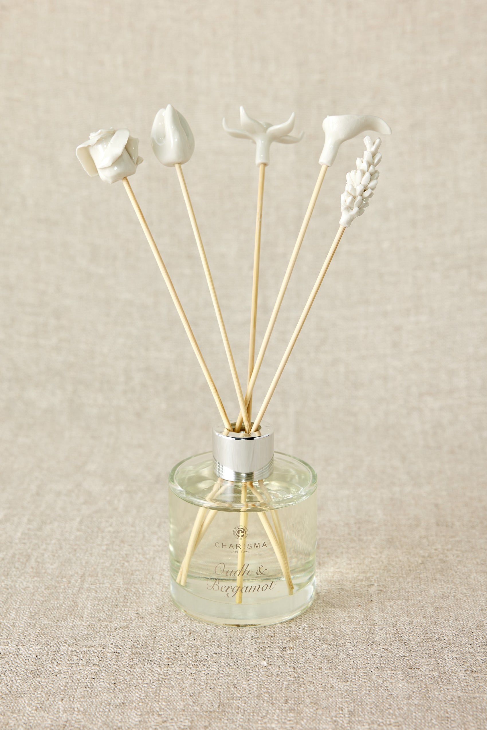 A set of white porcelain floral diffuser sticks placed in a clear glass container, with a beige background.