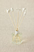 A set of white porcelain floral diffuser sticks placed in a clear glass container, with a beige background.