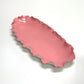 Pink ceramic dish with wavy edge on a white background