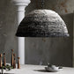 Textured pendant light hanging above a table with candles and a bowl in a rustic setting.