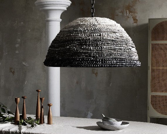 Textured pendant light hanging above a table with candles and a bowl in a rustic setting.