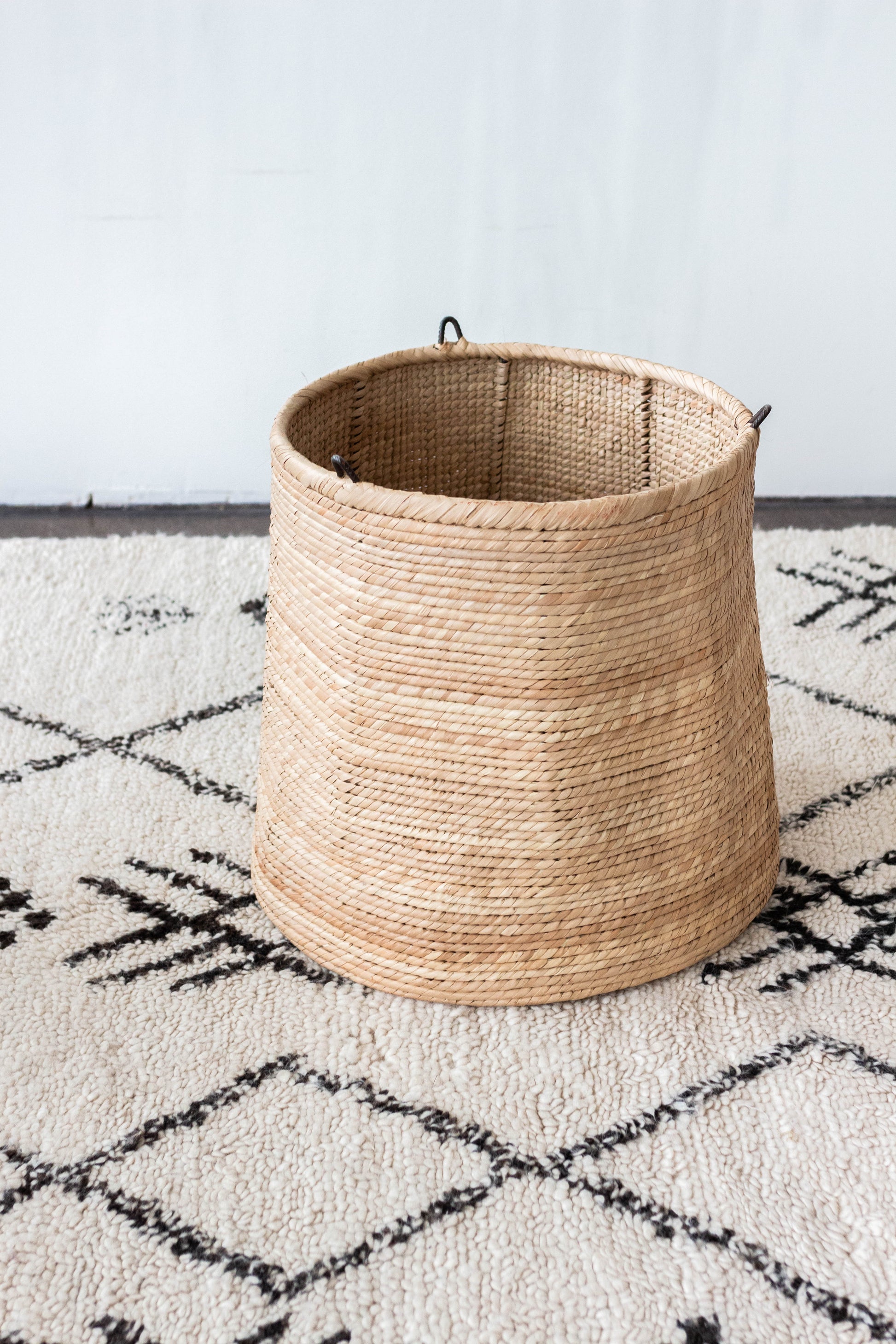 Woven basket on a patterned rug with a white wall background