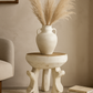 Decorative vase with dried pampas grass on a small table against a beige wall.