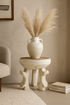 Decorative vase with dried pampas grass on a small table against a beige wall.