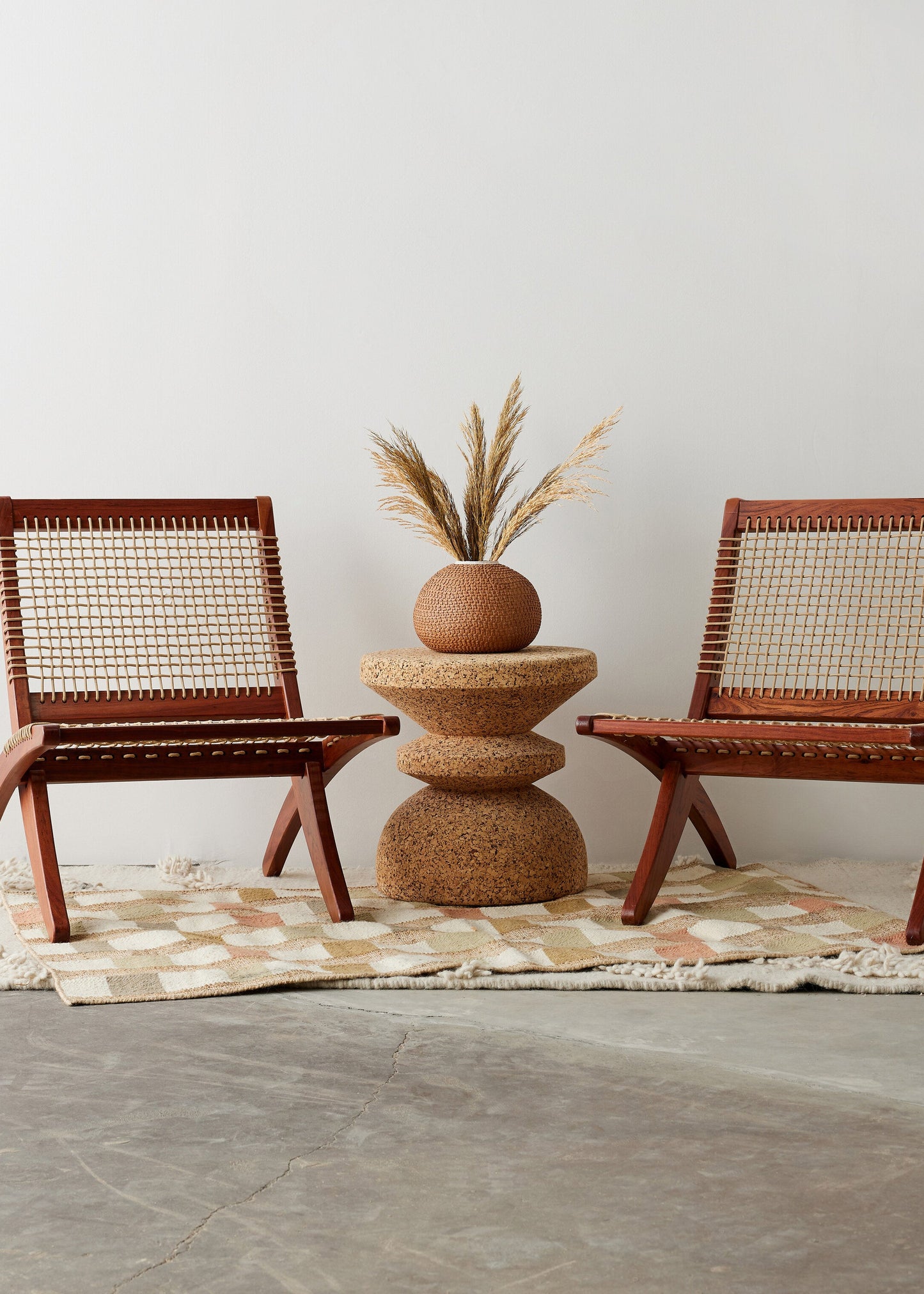 Two wicker chairs with a textured table and plant on a neutral rug.