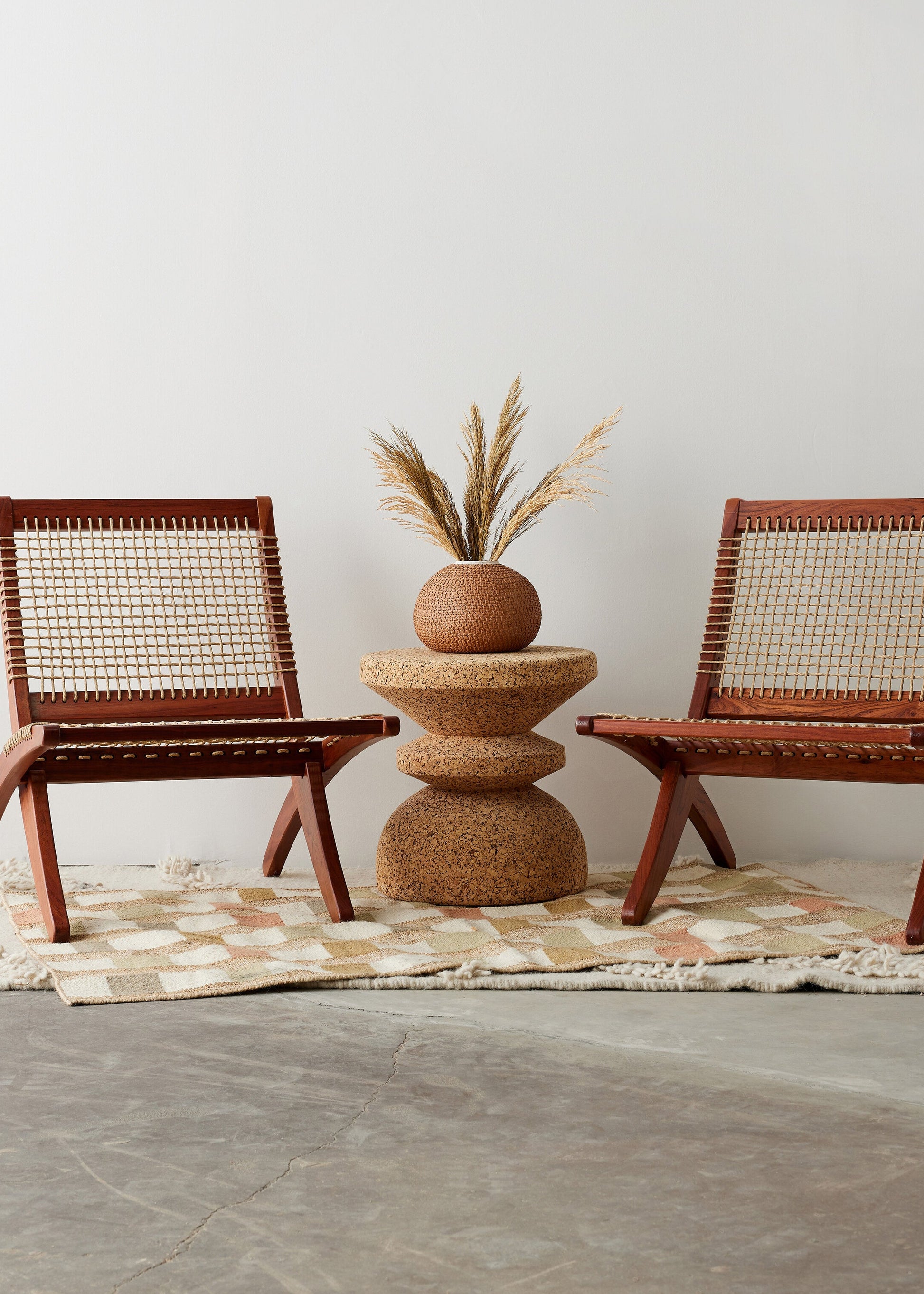 Two wicker chairs with a textured table and plant on a neutral rug.