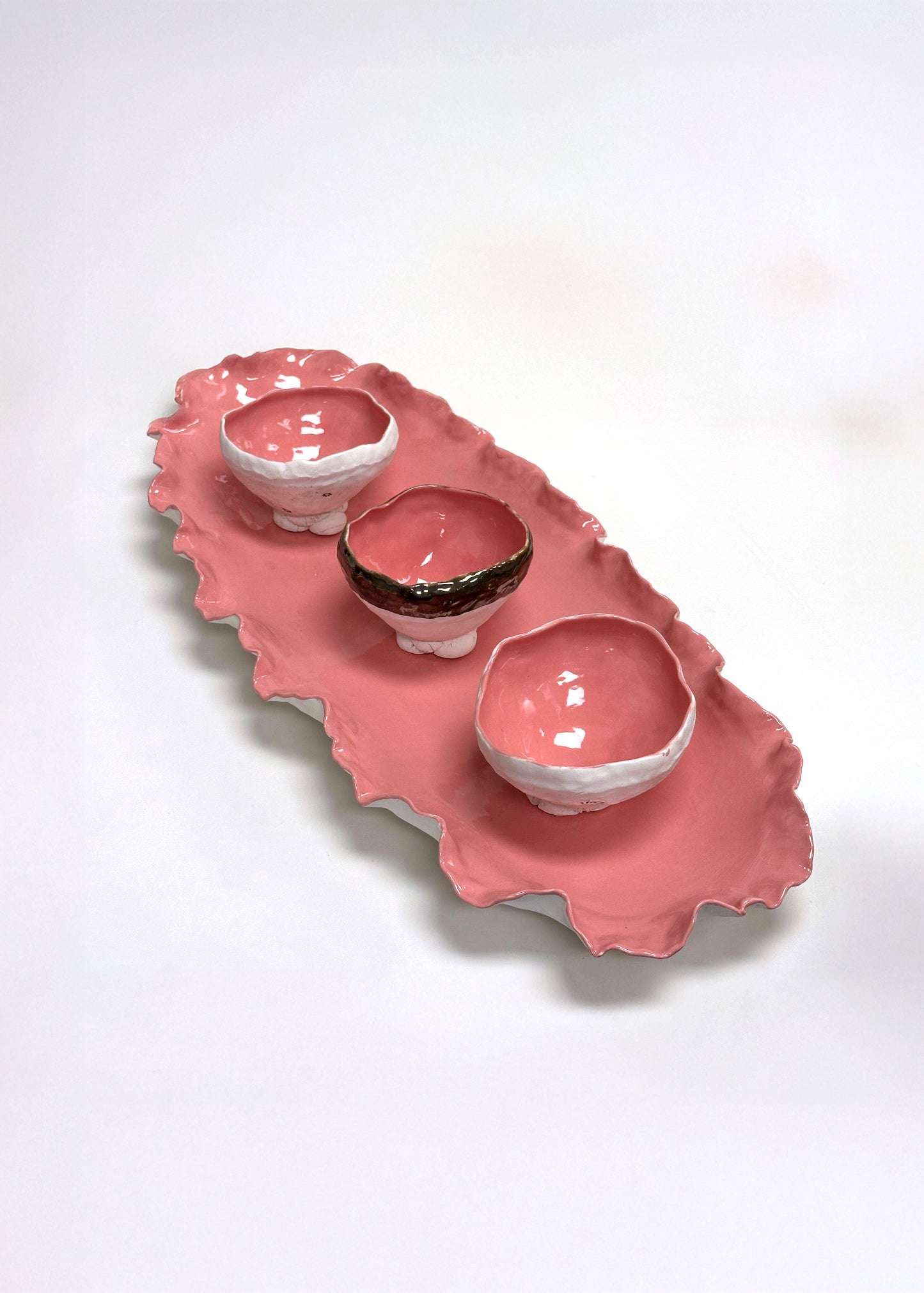Pink ceramic tray with three bowls on a white background