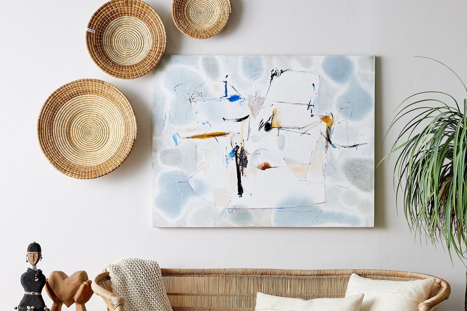 Living room with wicker furniture, decorative plates, and abstract art on a white wall.
