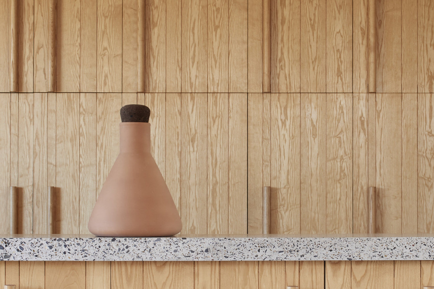 Ceramic vase on a countertop with wooden paneling and a stool in the background