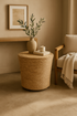 Woven side table with a plant, candle, and book in a cozy room.