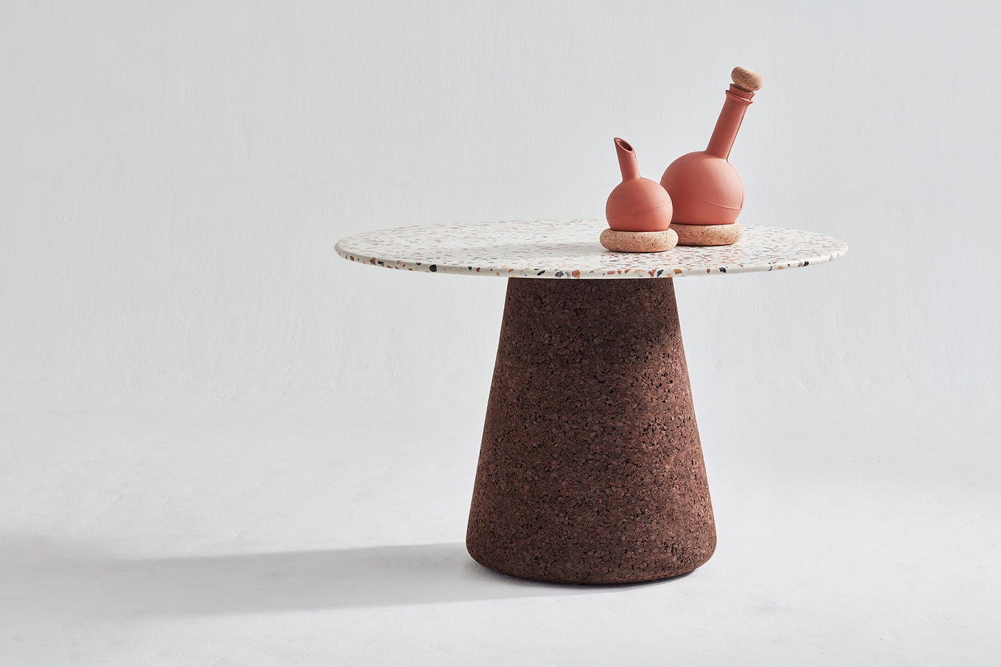 Product image of Kanju's Wiid Terrazzo and Cork Dining Table in Dark Cork, showcasing its sleek, modern design. The table features a luxurious terrazzo top with specks of vibrant colors, perfectly complemented by the rich, eco-friendly dark cork base. This piece epitomizes contemporary elegance, blending innovative materials with functional artistry, ideal for sophisticated dining spaces