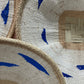 Three woven hats with blue decorative elements on a neutral background