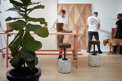 Contemporary work area elegantly styled with Kanju's Wiid Cork and Concrete Swivel Barstool in Terrazzo and Dark Cork, complemented by Wiid cork panels on the walls. This setup showcases a harmonious blend of textures and materials, highlighting the stool's unique design and the natural aesthetic of cork. The terrazzo base adds a splash of artistic detail, creating a functional yet inspiring workspace that emphasizes sustainability and modern style.