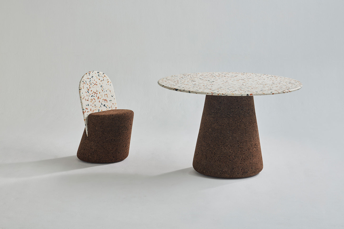 Elegant dining set from Kanju featuring the Wiid Design Terrazzo and Cork Dining Table in Dark Cork, paired with matching Wiid Design Terrazzo and Cork Dining Chairs. This sophisticated ensemble combines the unique beauty of terrazzo with the natural warmth of dark cork, offering a stunning example of sustainable luxury and innovative design. Ideal for those who appreciate artisan craftsmanship and eco-friendly materials in their dining space.