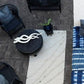 An outdoor seating area with a geometric patterned blue and white wool rug, surrounded by black furniture and decorative pillows.