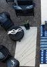 An outdoor seating area with a geometric patterned blue and white wool rug, surrounded by black furniture and decorative pillows.